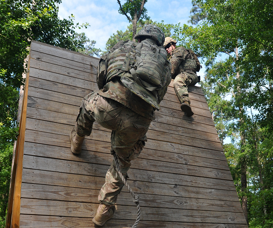 Photo of a soldier climbing a wood wall with a rope on a confidence course.
